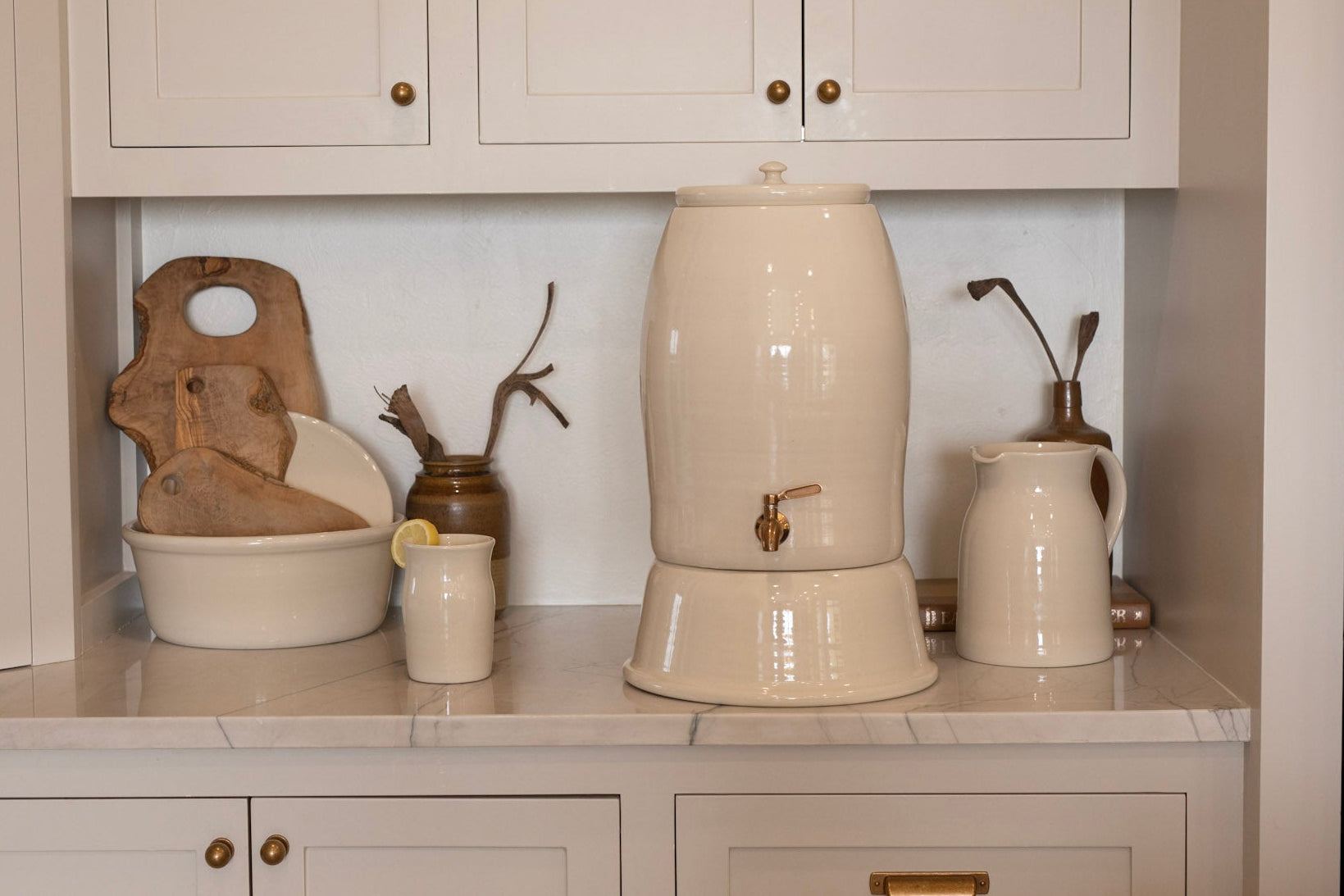Kitchen counter with ceramic water filter, ceramic cup, and ceramic pitcher.
