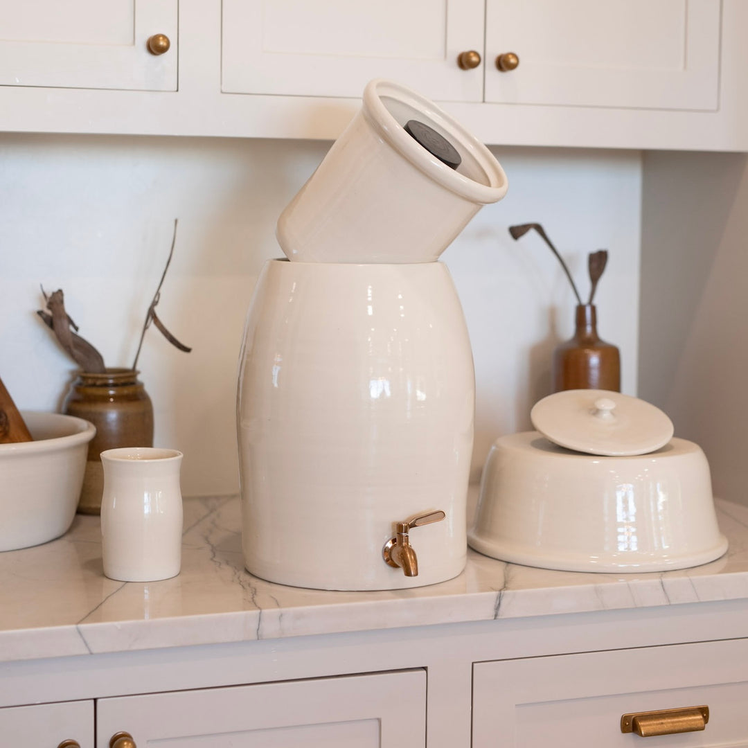 White ceramic water filter with a brass spigot on a kitchen counter