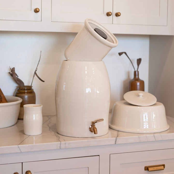 White ceramic water filter with a brass spigot on a kitchen counter