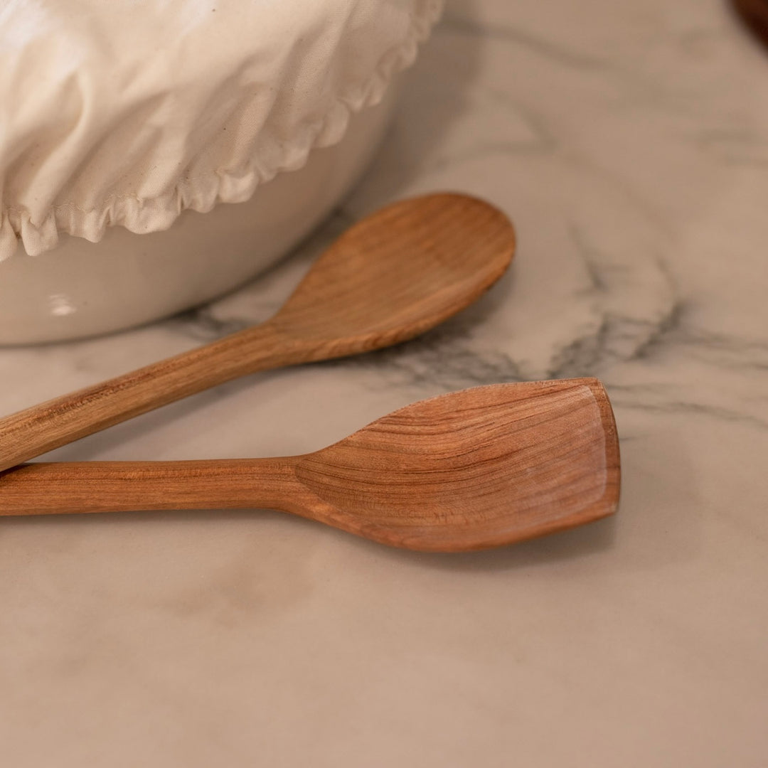 Two handmade wooden serving spoons on a marble kitchen counter.