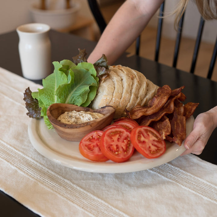 Ceramic board with bread, bacon, tomatoes, garden lettuce, and herb mayo sauce being served.