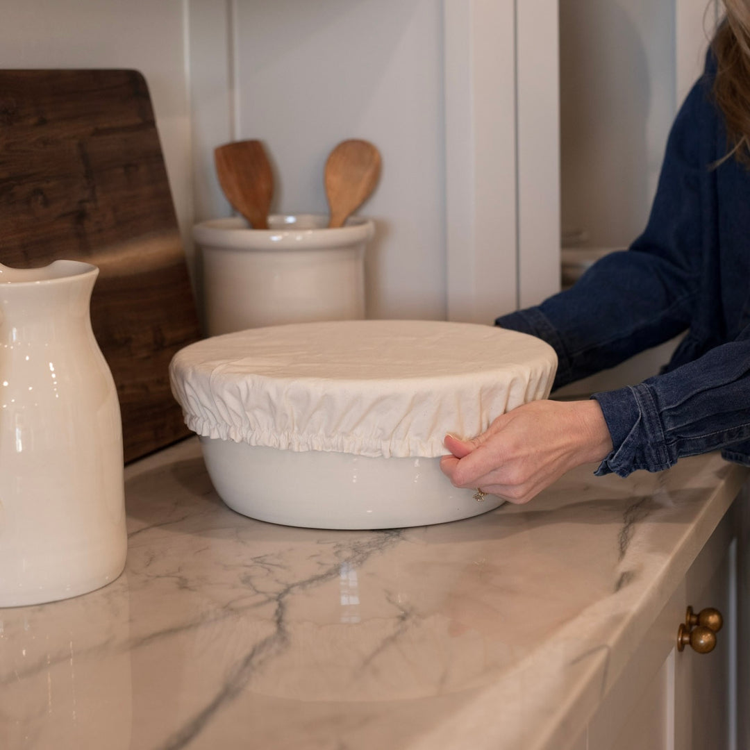 Person covering a beautiful ceramic bowl for bread baking with a natural cotton bowl cover.
