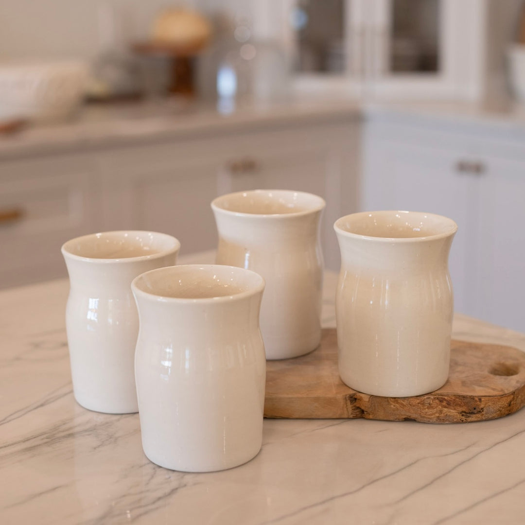 Four white ceramic cups on a wooden tray with a kitchen background
