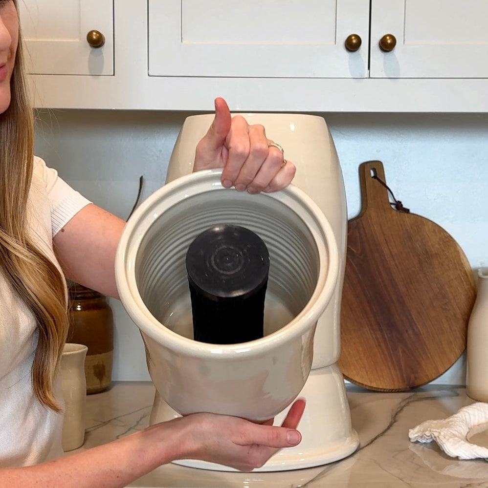 Person holding a ceramic crock with a gravity water filter cartridge in kitchen