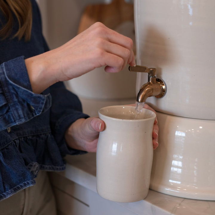 Person filling a ceramic drinking glass with water from a water filter